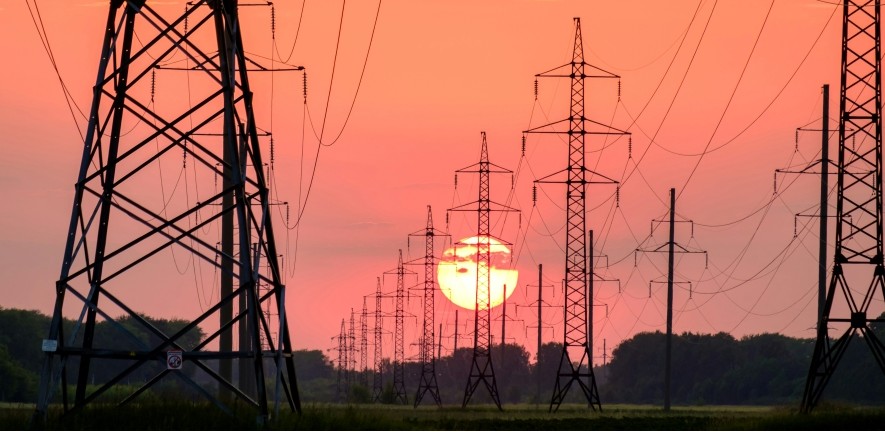 The image shows power lines stretching between rows of pylons at the end of a sunny day